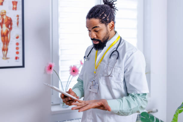 Cardiologist engaged with medical tech An image showcasing a focused African-American cardiologist in his lab coat, deeply engaged with a digital tablet, highlighting the role of technology in cardiac care male nurse male healthcare and medicine technician stock pictures, royalty-free photos & images