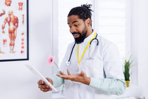 Pediatrician embraces modern medical tech A warm portrait of an African-American pediatrician using a digital tablet in his clinic, representing the blend of traditional care with modern technology male nurse male healthcare and medicine technician stock pictures, royalty-free photos & images