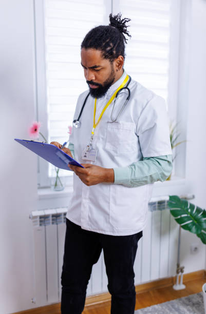 General practitioner updating patient records An engaging scene showing a general practitioner in a lab coat, writing on a document with a pen, showcasing the thoroughness and attention to detail required in medical practice male nurse male healthcare and medicine technician stock pictures, royalty-free photos & images