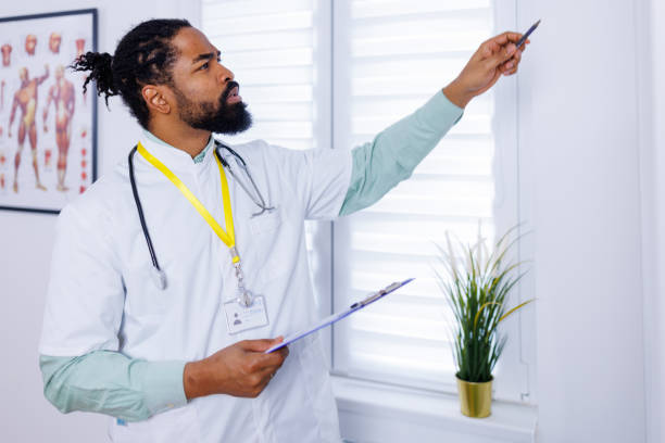 Medical professional engaged in paperwork An image of a medical professional, standing in a clinic, pen in hand, focused on paperwork, symbolizing the administrative aspect of healthcare management male nurse male healthcare and medicine technician stock pictures, royalty-free photos & images