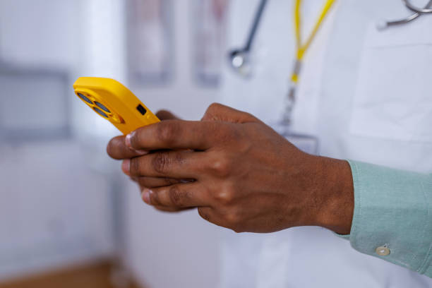 Healthcare professional's mobile tech use A scene depicting a healthcare worker, a mid-adult man, adeptly using a mobile phone for work purposes, highlighting the blend of medical expertise and modern communication tools male nurse male healthcare and medicine technician stock pictures, royalty-free photos & images