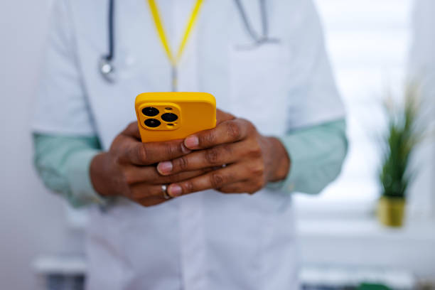 Surgeon staying connected with smartphone A portrait of a surgeon, smiling while looking away from the camera, as he holds a smartphone, emphasizing the importance of staying connected and informed in the medical field male nurse male healthcare and medicine technician stock pictures, royalty-free photos & images