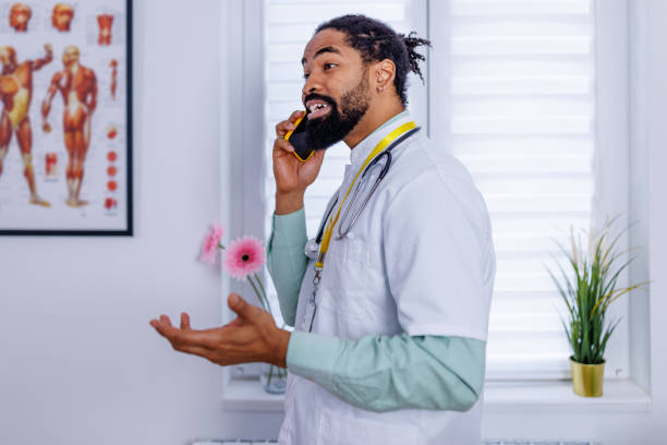 Healthcare worker's mobile communication A portrait showcasing a healthcare worker, a mid-adult man, talking on his mobile phone, reflecting the dynamic integration of wireless technology in healthcare environments male nurse male healthcare and medicine technician stock pictures, royalty-free photos & images