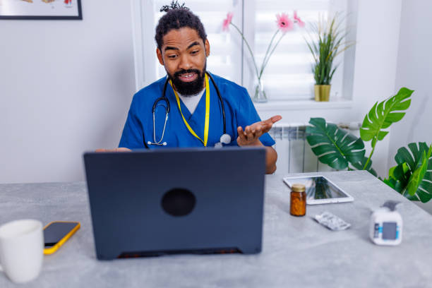 Male nurse's vital role in telehealth A photo depicting a male nurse intently using a laptop for a telehealth session, underscoring the essential role of nursing professionals in digital healthcare services male nurse male healthcare and medicine technician stock pictures, royalty-free photos & images