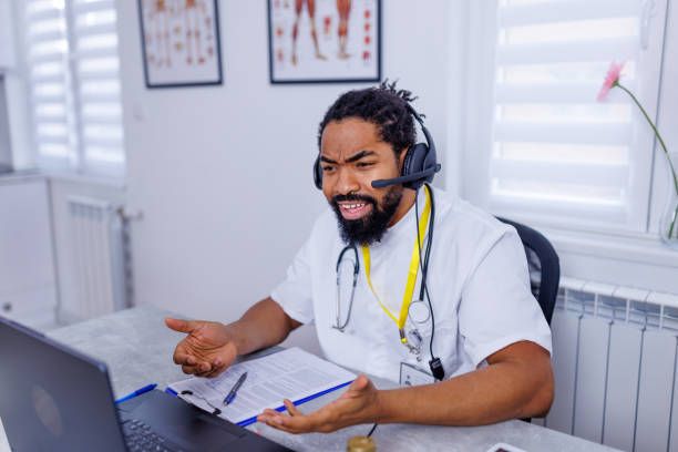 Healthcare professional's efficient telehealth setup A portrait of a healthcare professional, using a headset during a laptop-based telemedicine session, emphasizing efficiency and clarity in virtual patient interactions male nurse male healthcare and medicine technician stock pictures, royalty-free photos & images