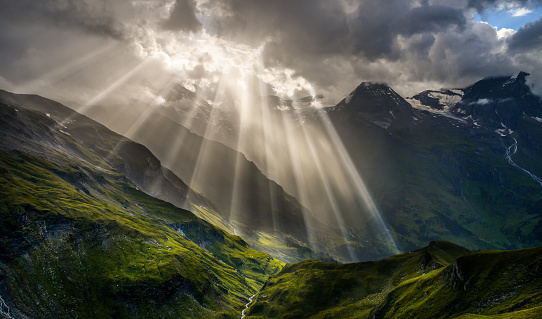 Landscape and nature in the spring. Landscape with dramatic sky and green meadows. The sun rays through the clouds. The Hohe Tauern mountain range, the valley below the hochalpenstrasse and in the background the highest peak of the grossglockner.