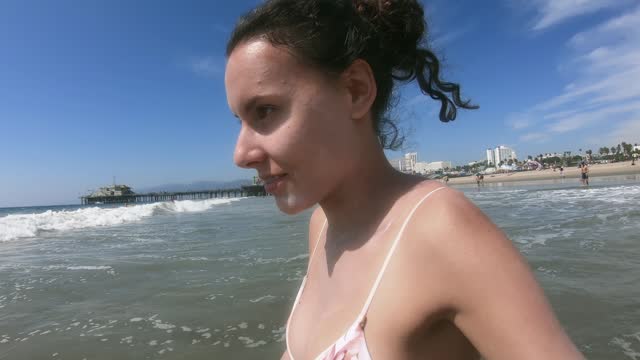 Young woman getting into the ocean while on vacation in California, near the famous Santa Monica Wheel on the pier