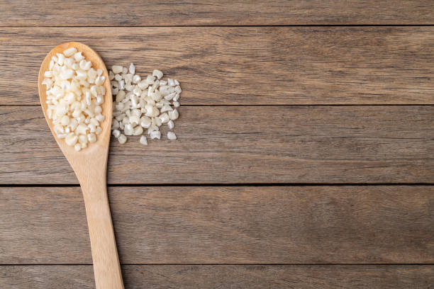 Dried canjica, hominy or white corn on a spoon over wooden table with copy space.