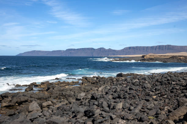 istock Coast with lava stonesl and a mountain, Lanzarote, Spain 1907717384