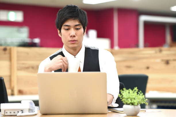 istock Asian young male office worker working on laptop while having a drink indoors 1907719437