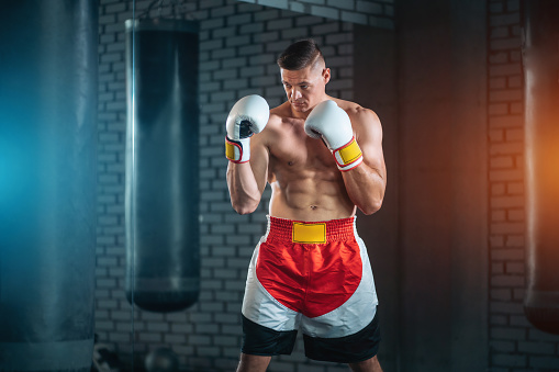 muscular sport man exercising and fight with punching bag indoor