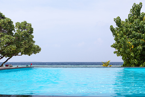 Photo of infinite pool with blue water and perfect sea view. Dream vacation in luxury resort. Edgeless swimming pool