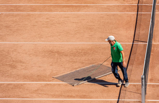 Brasov, Romania - September 02 2023: A man clean sweeping the tennis court clay surface.