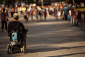 Disabled man sitting in wheelchair driving along the street among other people. The concept of living life to the fullest. Blurred focus.