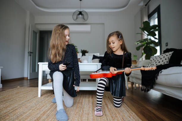 Funny adorable happy kid girls player guitars and sing in microphone. Two happy beautiful caucasian laughing little girls playing guitar and applauding at home