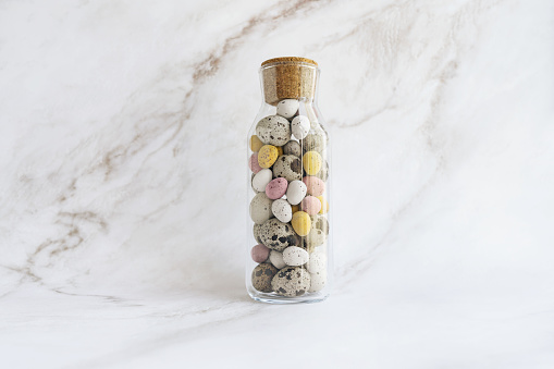 Easter decor for home. glass spice bottle full of chocolate eggs and colored quail eggs sits on marble countertop. DIY Easter home decor concept, minimalism, pastel colors, spring holiday, holiday