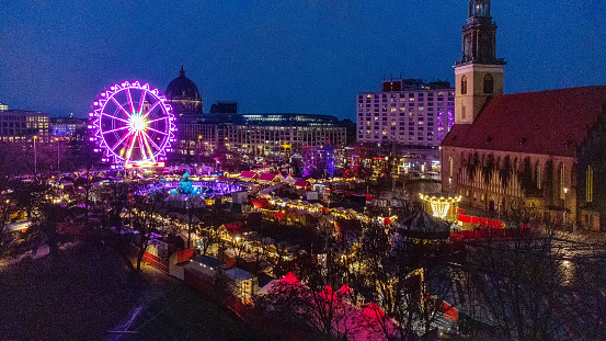 Amazing drone point of view on Christmas market next to St. Mary's Church and Berlin Fernsehturm in blue hour in evening Berlin with Christmas lights of marlet stalls