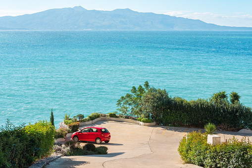 Car on a sea coast. Red car on the road near the ocean on sunny summer day. Red car parked at the beach. Summer vacation at the beach. Summer travel by car. Road trip. Automotive industry.