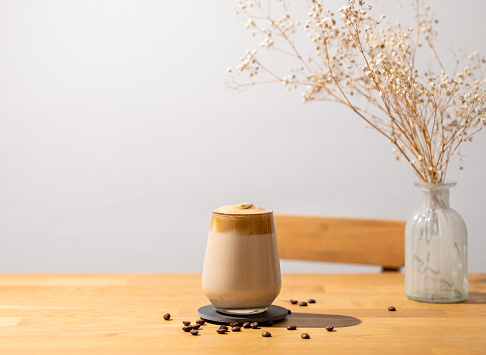 Dalgona coffee. Whipped instant coffee in a glass with beans on a wooden background with dry bouquet.  The concept of a trendy and popular drink.