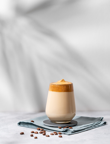 Dalgona coffee. Whipped instant coffee in a glass with beans and shadow on a light background.  The concept of a trendy and popular drink.