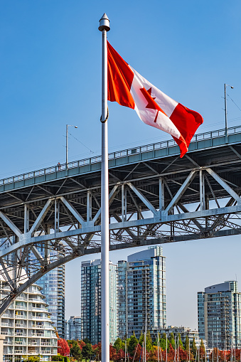 Canadian flag with downtown Vancouver in background. Location is Granville Island. Flag of Canada in front of view of False Creek and the Burrard street bridge in Vancouver, Canada