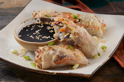 Asian deep fried spring roll filling with tofu, cabbage, carrot and glass noodle on natural plate eating with dipping sauce. Vegan food