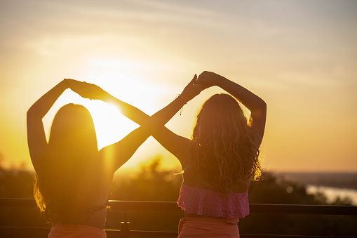 teenage girls are playing at sunset and are happy making sign infinite with hands