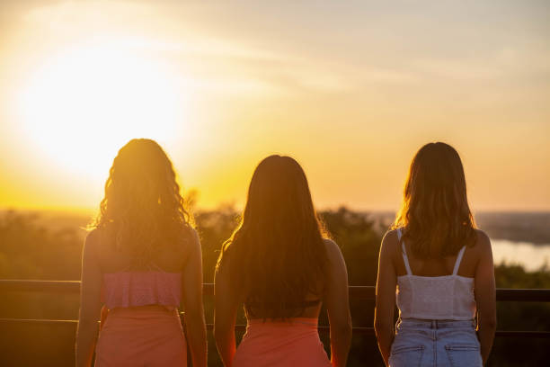 three girls standing together on the terrace watching the sunset in their bathing suits