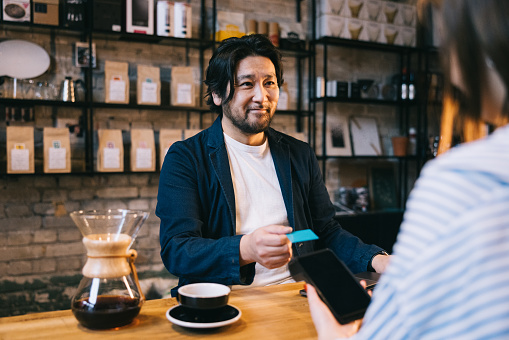 Japanese businessman taps his card for a contactless payment at a cafe, showcasing the efficiency and ease of modern payment