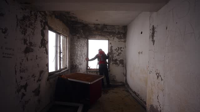 Traveling man with backpack explores abandoned ruined house