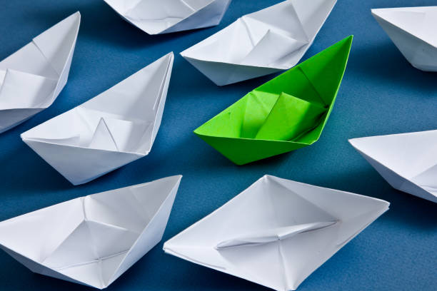 istock White paper boats with one green on blue background from above 1907944675