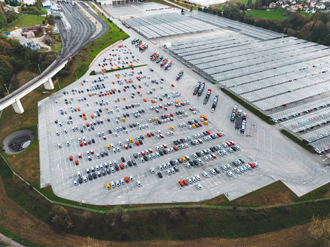 Drone view over large outdoor parking lot, aerial view of massive parking lot for cars and trucks, accommodating an extensive array of cars and trucks in a spacious parking spot