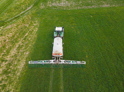 Aerial view of modern tractor working on the agricultural field, top view of tractor plowing and sowing on a grassy field, cultivation of agricultural land