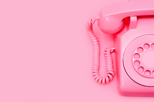 A pink old fashioned rotary style phone, photographed on a matching pink colored backdrop for a monochromatic style.