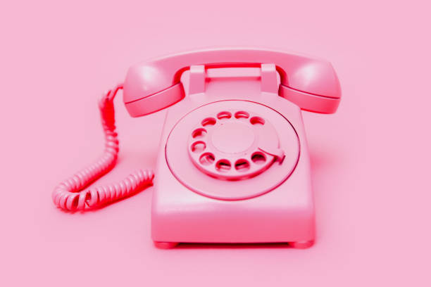 A pink old fashioned rotary style phone, photographed on a matching pink colored backdrop for a monochromatic style.