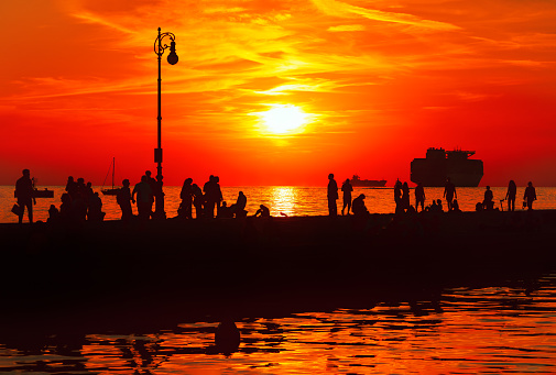 Silhouette of people on the pier at sunset in summer . Scenic and atmospheric coastal scene with people in the twilight