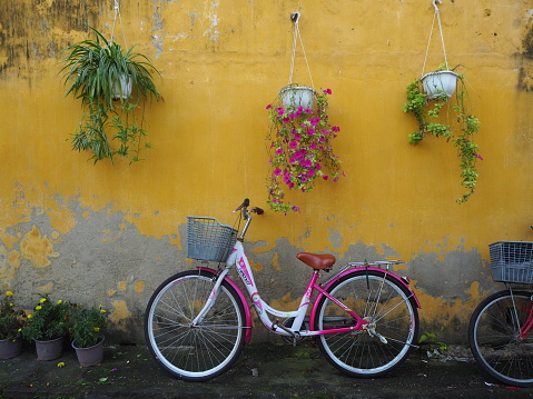 Pink and white ladies bicycle leaning against yellow wall with peeling paint