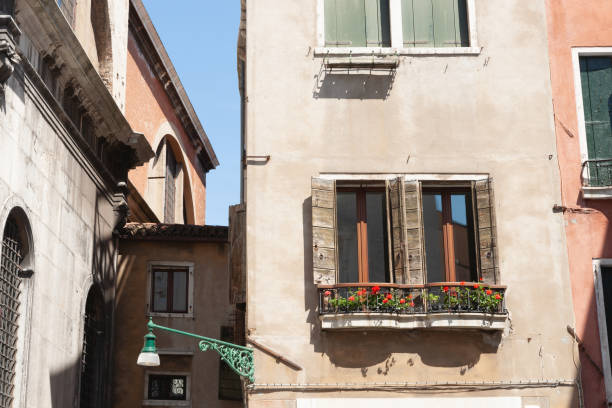 istock Red geranium flowers in window with shutters in rustic exterior wall in Venice 1908057658