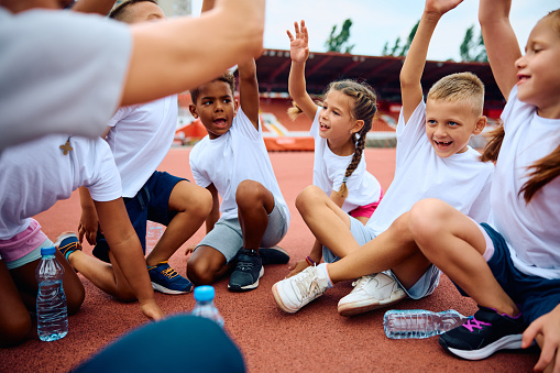Multiracial group of children greeting with hands raised during exercise class at athletics club.
