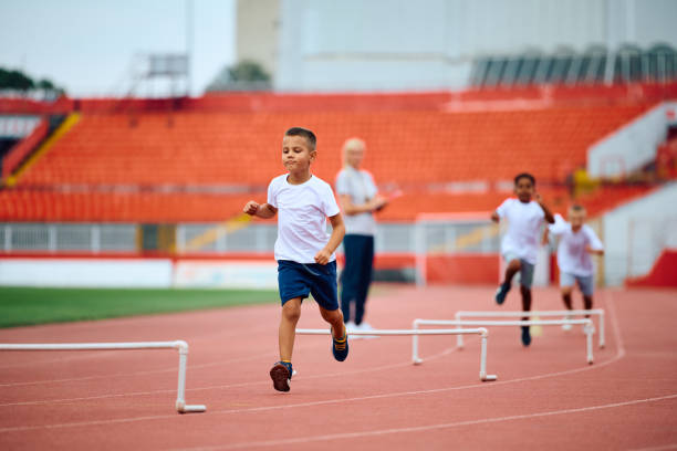 istock Little boy jumping over obstacles while running on a track at athletics club. 1908079867