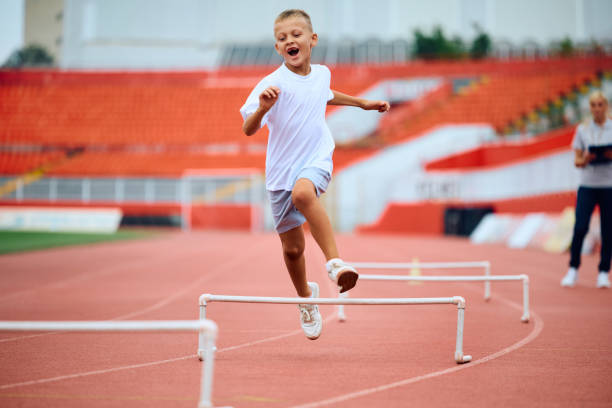 istock Cheerful kid umping over obstacles while running during sports training at the stadium. 1908080381