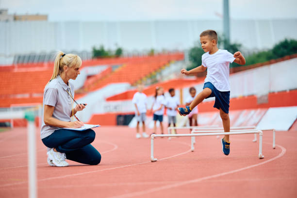 istock Kid jumping over obstacles during PE class at the stadium. 1908081424