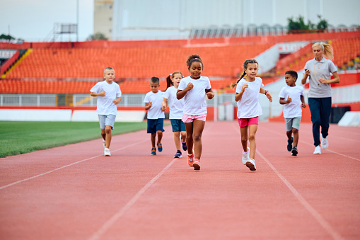 Group of kids running on a track during exercise class at athletics club.