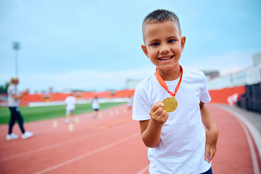 Happy kid with golden medal at the stadium looking at camera.. Copy space.