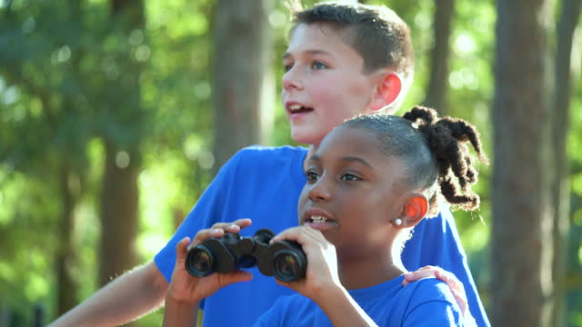 Two multiracial children exploring park with binoculars