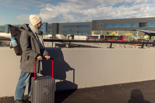 A female tourist with a suitcase and a backpack on her back is standing near the airport