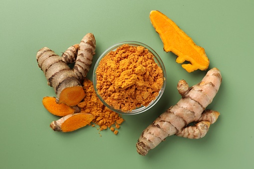 Aromatic turmeric powder and raw roots on green background, flat lay