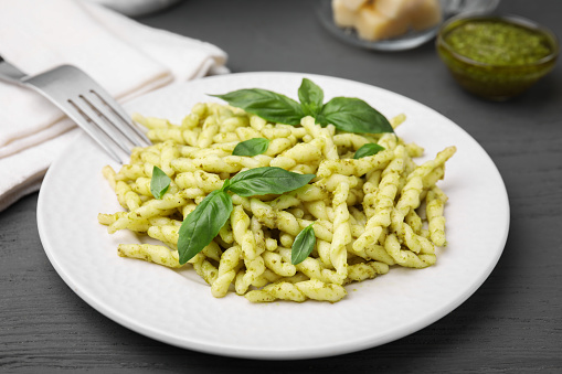 Plate of delicious trofie pasta with pesto sauce and basil leaves on grey wooden table