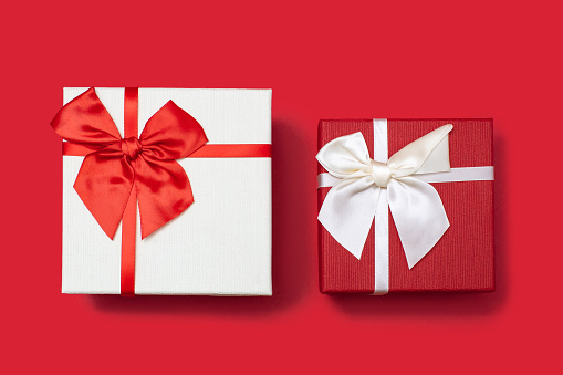 Two white and red gift boxes with ribbons and bows on a red background. Gifts for birthday or traditional holidays. Two gift boxes close up