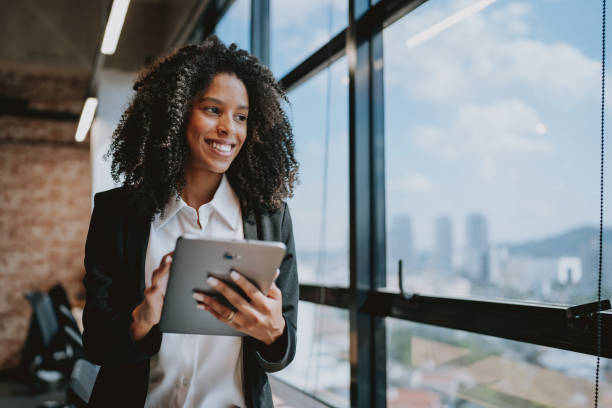 istock Young businesswoman using digital tablet looking at window view 1908372051